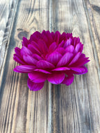 A single vibrant magenta-purple dahlia flower resting on a rustic, weathered wooden plank surface.